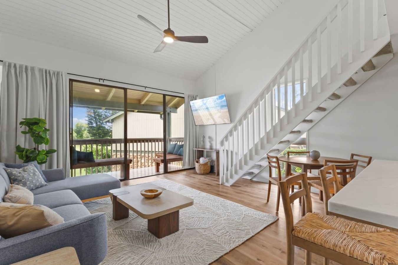 A spacious living area with a sofa, coffee table, and dining table, a staircase, and a television.