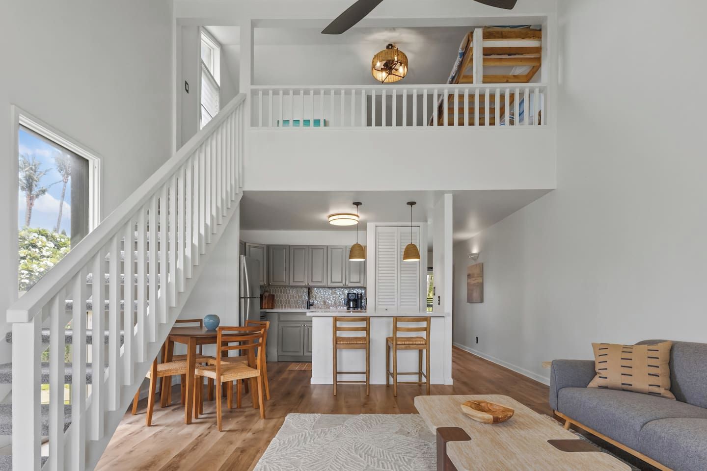 A spacious living area with a high ceiling, a dining table with chairs, a sofa, and a kitchen in the background.