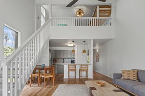 A spacious living area with a high ceiling, a dining table with chairs, a sofa, and a kitchen in the background.