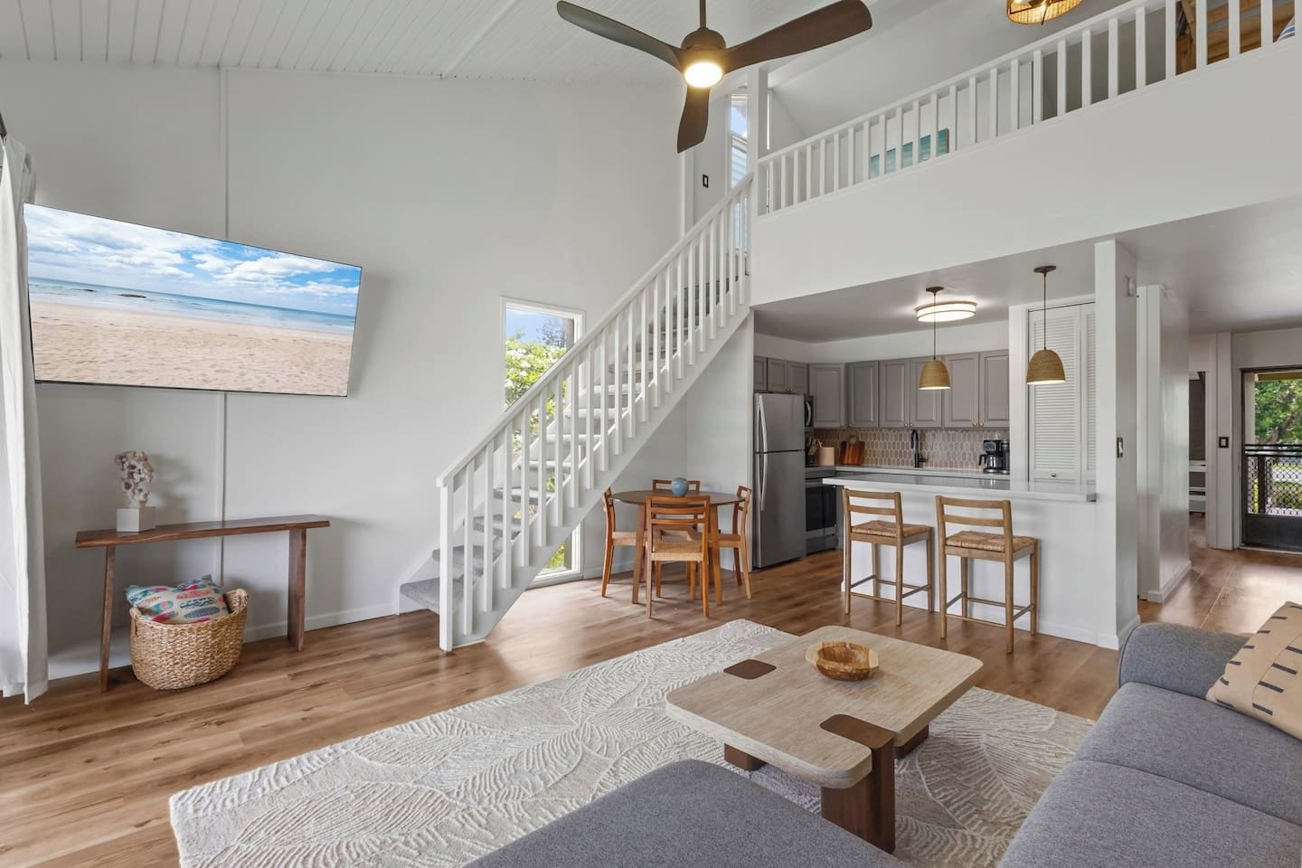 A spacious living area with a high ceiling, a staircase, a kitchen, and a dining area.