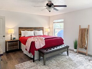 A bedroom with a bed, bedside tables, a bench, a ceiling fan, and a window. - Donnelly Mountain Retreat | Games, Wood Stove & Fire Pit (Donnelly)
