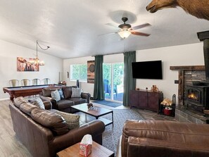 A living room with a pool table, leather sofas, a fireplace, and a television. - Donnelly Mountain Retreat | Games, Wood Stove & Fire Pit (Donnelly)
