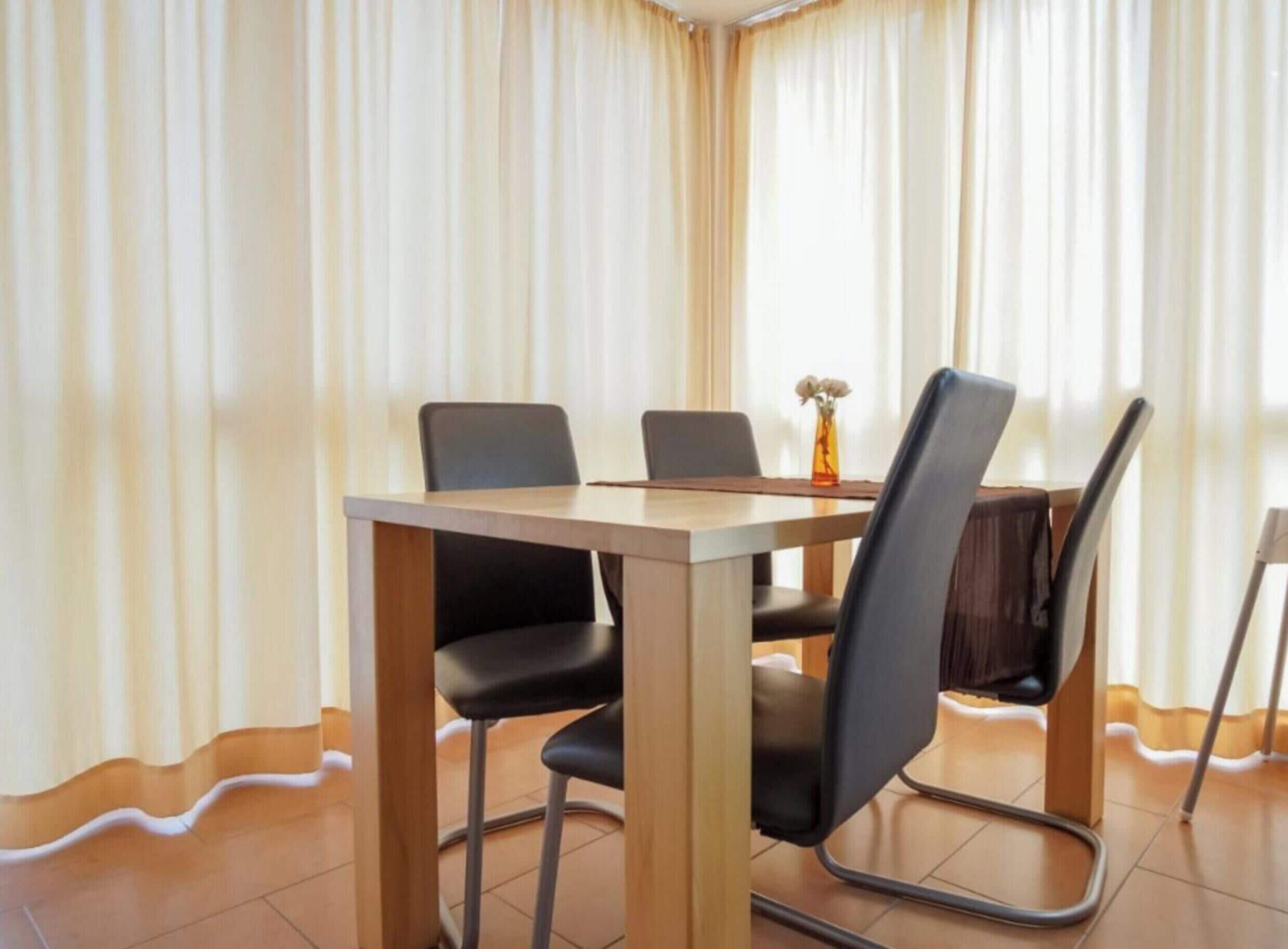 Una habitació amb taula de dinar, quatre cadires i un vas amb flors.