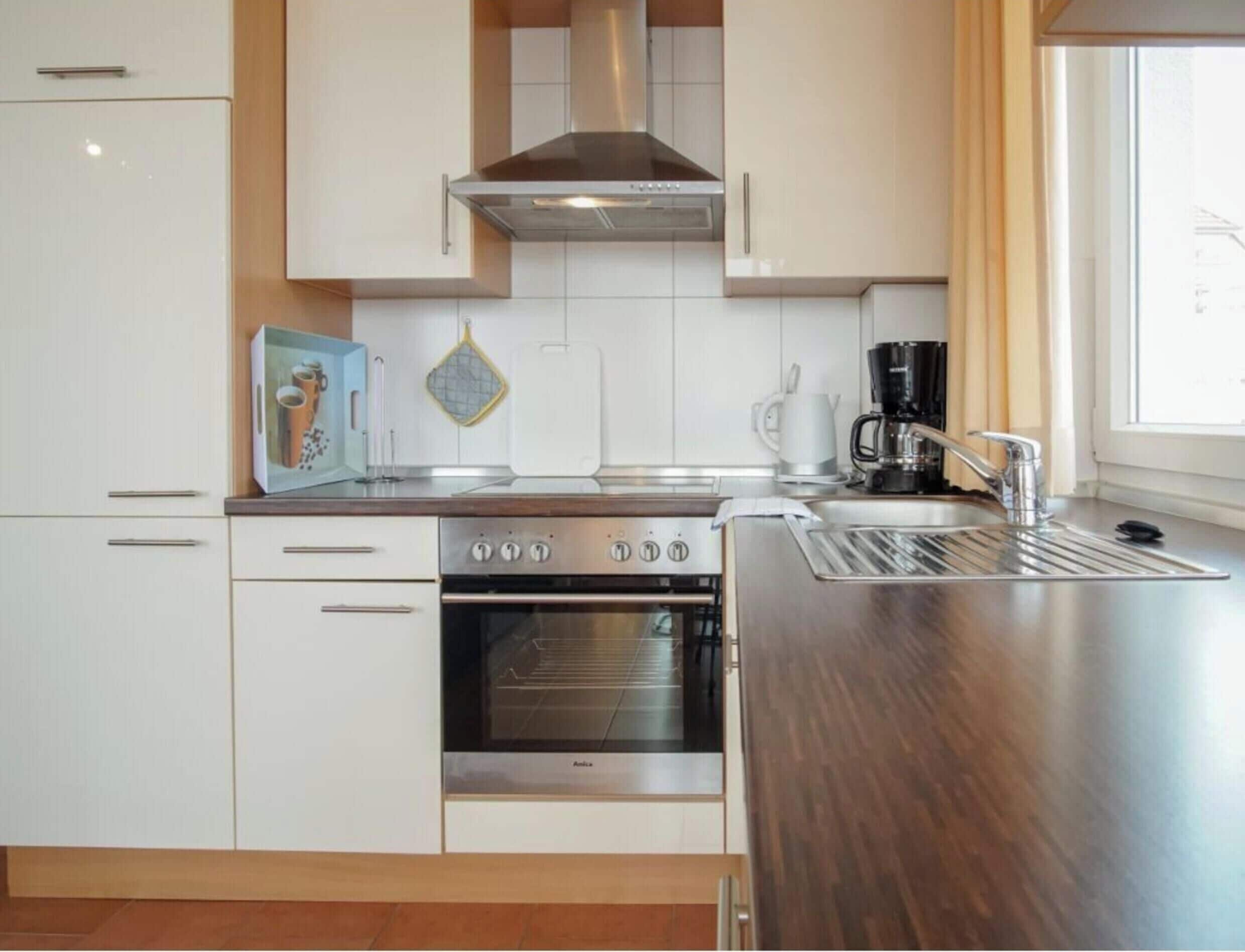 Una cocina moderna con armarios blancos, electrodomésticos de acero inoxidable y un ventanal que proporciona luz natural.