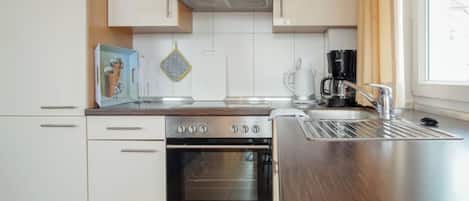 Una cocina moderna con armarios blancos, electrodomésticos de acero inoxidable y un ventanal que proporciona luz natural.
