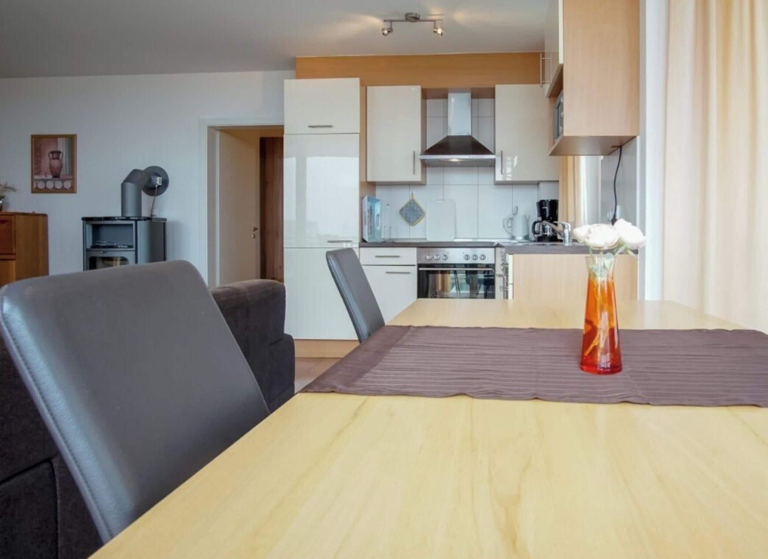 Una cocina moderna con gabinetes blancos, estufa y cafetera. Hay una mesa de comedor con un florero.
