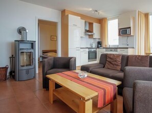 A compact living space with a kitchenette, a sofa, a table, and a wood-burning stove. - Holiday Apartment With 2 Bedrooms (Grossenbrode)