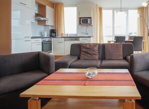 Een moderne woonkamer met een bank, een salontafel en een keuken op de achtergrond.