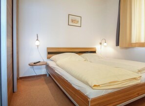 A single bed with a wooden headboard, two bedside lamps, a small bedside table with a remote control, and a framed picture on the wall. - Holiday Apartment With 2 Bedrooms (Grossenbrode)