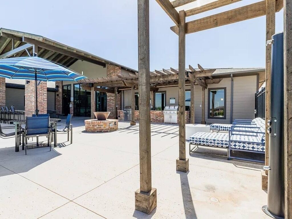 Un patio al aire libre con arreglos de asientos, una parrilla y una pérgola.
