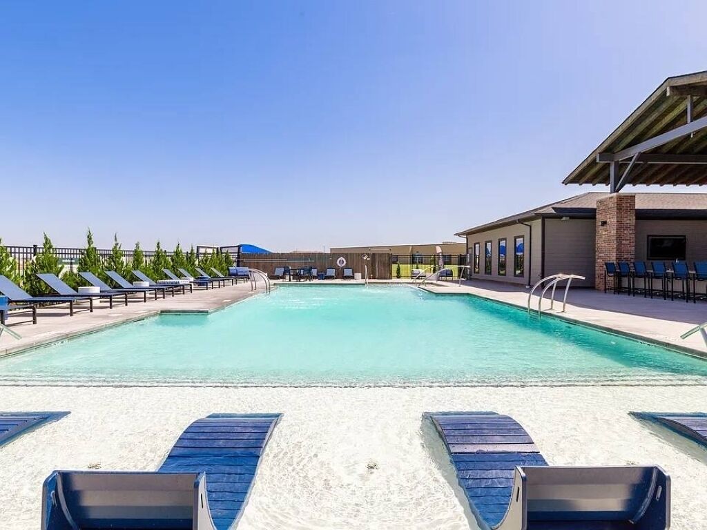 Una piscina con sillas de descanso y un edificio al fondo.