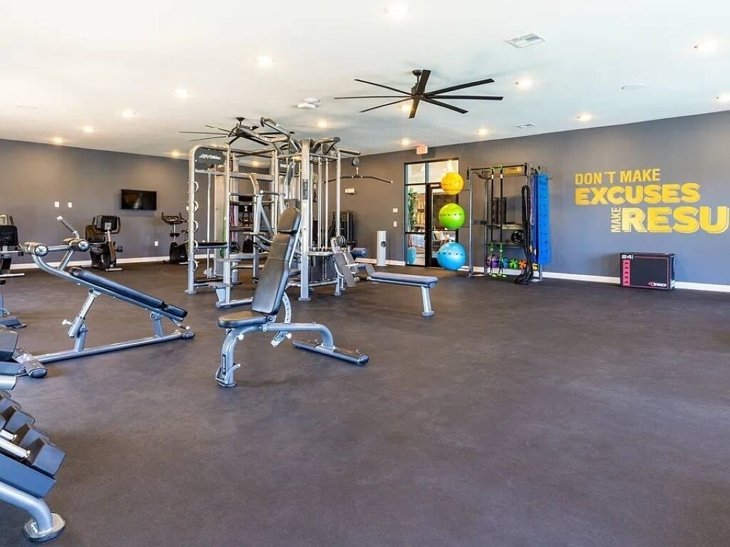 Ein Fitnessstudio mit verschiedenen Trainingsgeräten, einer motivierenden Wand und einem Deckenventilator.