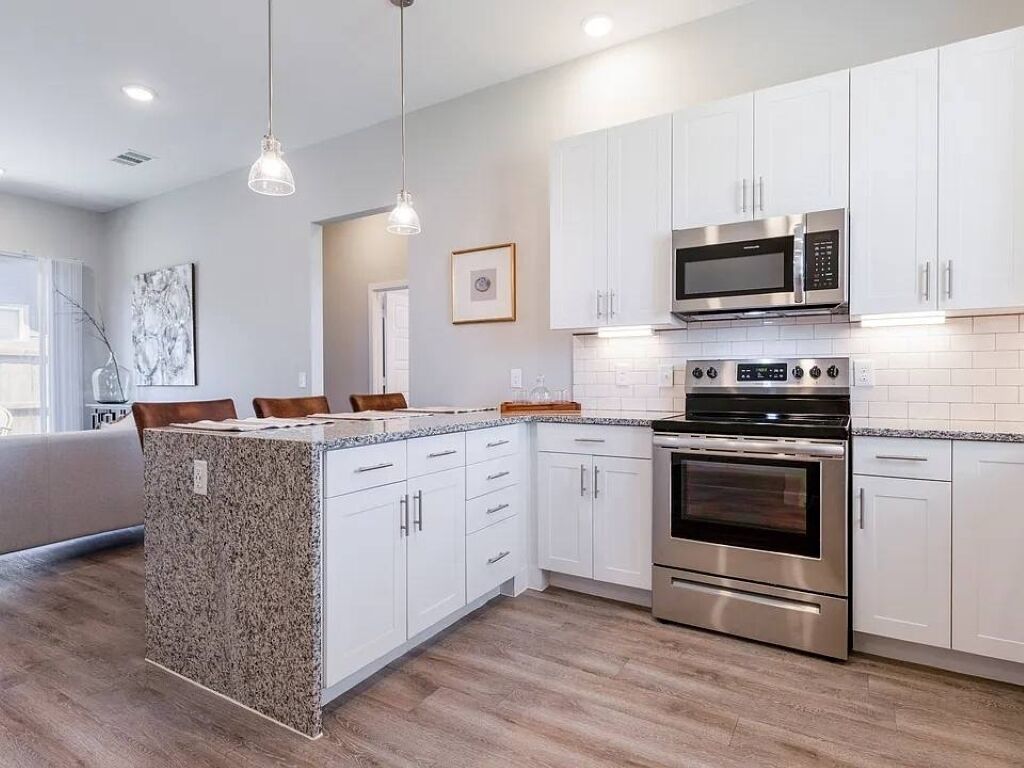 A modern kitchen with white cabinetry, stainless steel appliances, and a granite island.