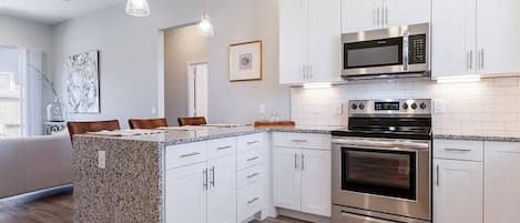 A modern kitchen with white cabinetry, stainless steel appliances, and a granite island.