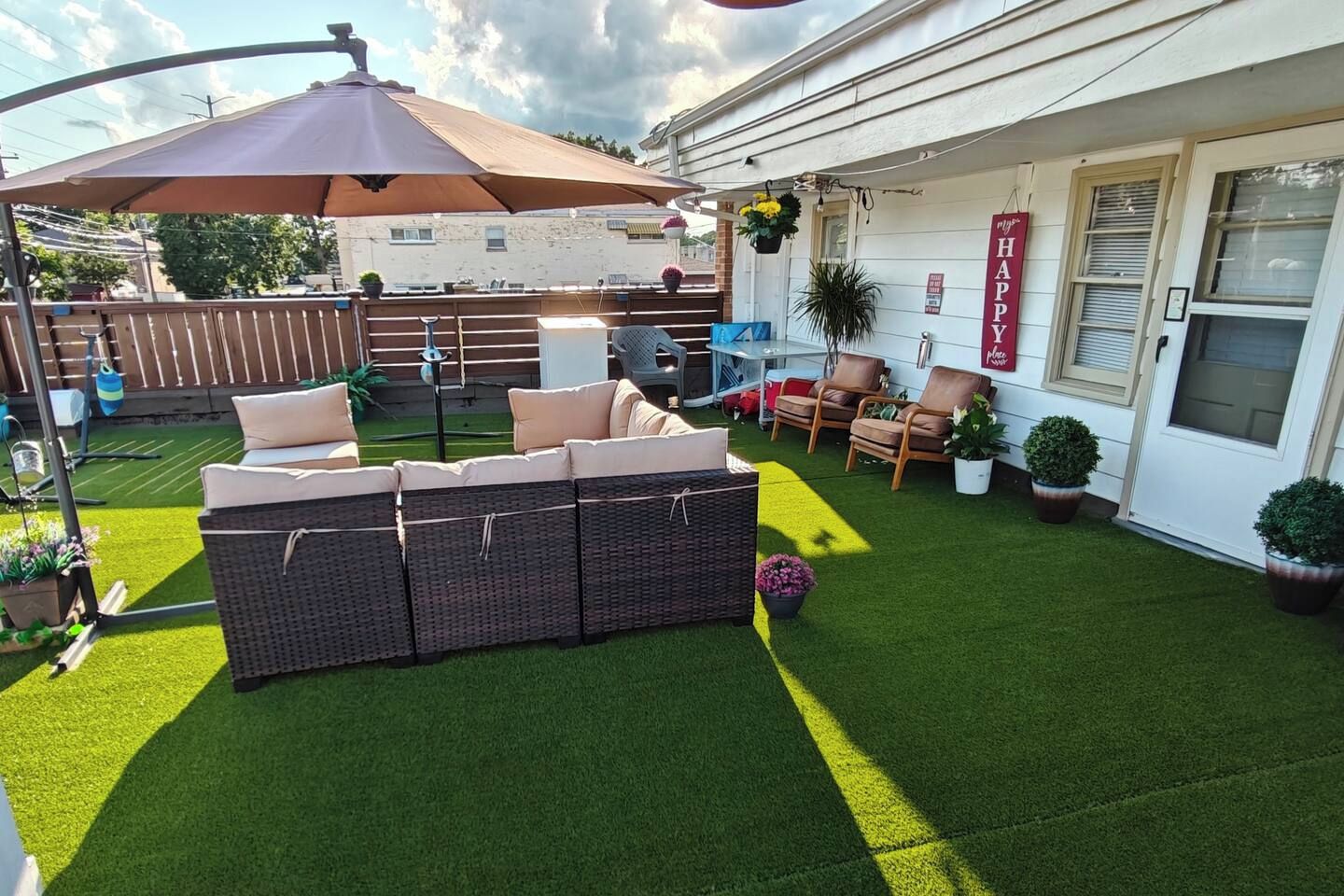 A patio with artificial grass, a wicker sofa, and a large umbrella.