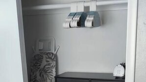 A room with a wooden floor, a grey storage unit with multiple drawers, and a patterned ironing board.