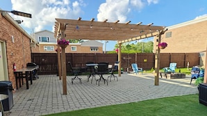 A backyard patio with a pergola, outdoor furniture, and a well-maintained lawn. - The Rooftop - Haven! (Waukegan)