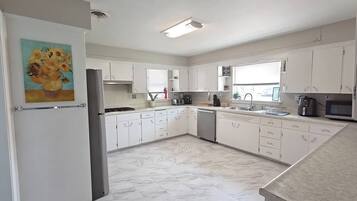 A modern kitchen with white cabinets, a marble floor, and a painting of sunflowers.