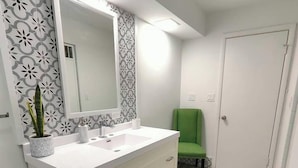 A bathroom with a white vanity, a large mirror, a green chair, and patterned wallpaper. - The Rooftop - Haven! (Waukegan)