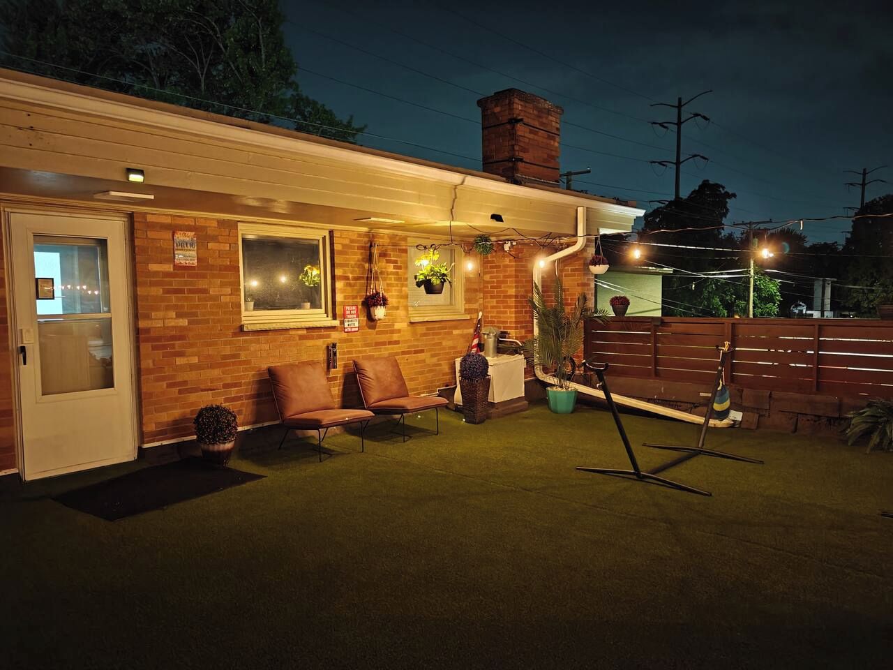 A well-lit patio area with a brick wall, a door, a bench, and potted plants.