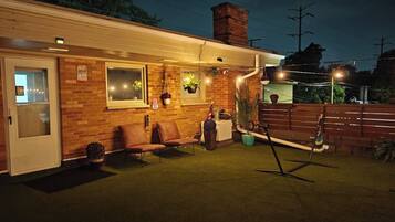 A well-lit patio area with a brick wall, a door, a bench, and potted plants.