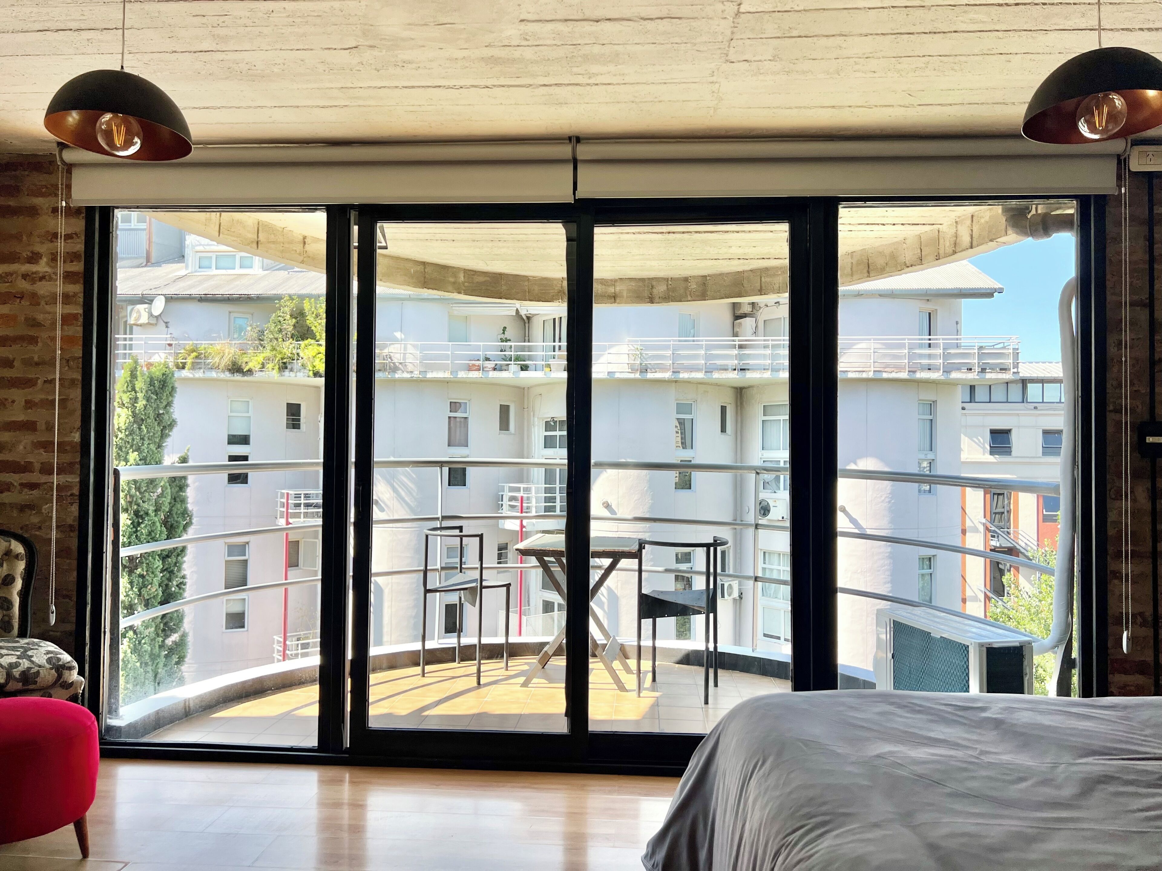 Une chambre dotée d’une grande porte-fenêtre coulissante donnant sur un balcon avec vue sur un immeuble d’habitation.