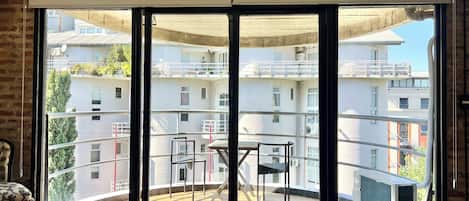 Un dormitorio con un amplio ventanal corredero que da a un balcón con vistas a un edificio residencial.