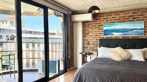 Ein Schlafzimmer mit einem großen Fenster, einem Bett, einem Kopfteil, einer Wand-Klimaanlage und einem Meeresblick-Gemälde.
