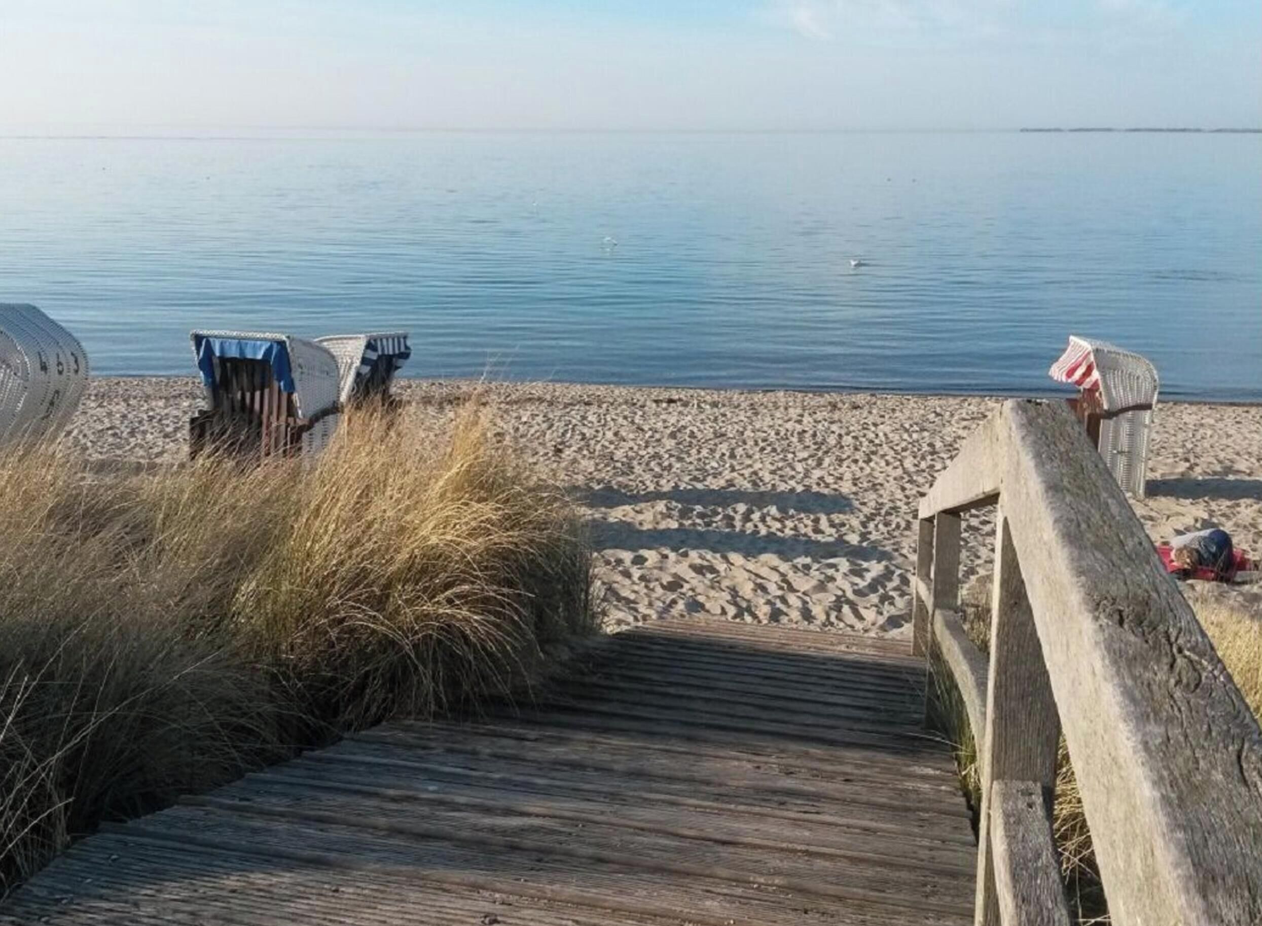 Een houten looppad dat naar een zandstrand leidt, met rustig water op de achtergrond.