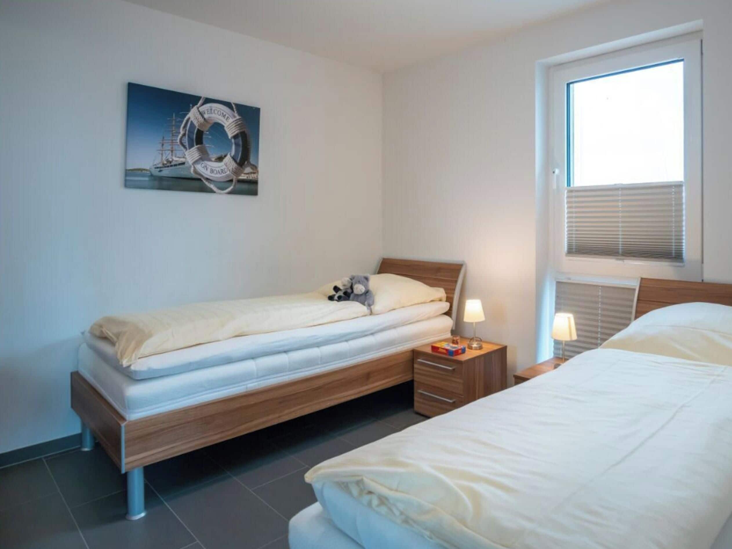Une chambre avec deux lits, une table de chevet avec une lampe, une fenêtre avec des stores et un tableau accroché au mur.
