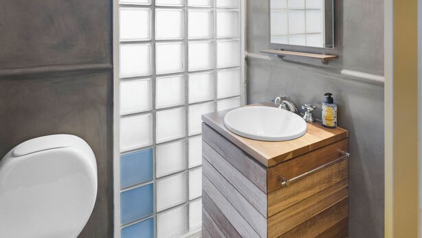 Ein Badezimmer mit Toilette, einem Waschbecken mit Holzschrank, einem Spiegel und einer Milchglasscheibe.