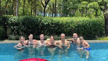 A group of people in a swimming pool with a red inflatable ring, surrounded by lush greenery.
