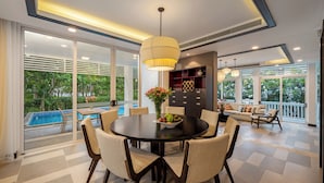 A modern dining area with a round table, chairs, a vase with flowers, and a pool view. - President Garden Ocean Villa  (Da Nang Municipality)