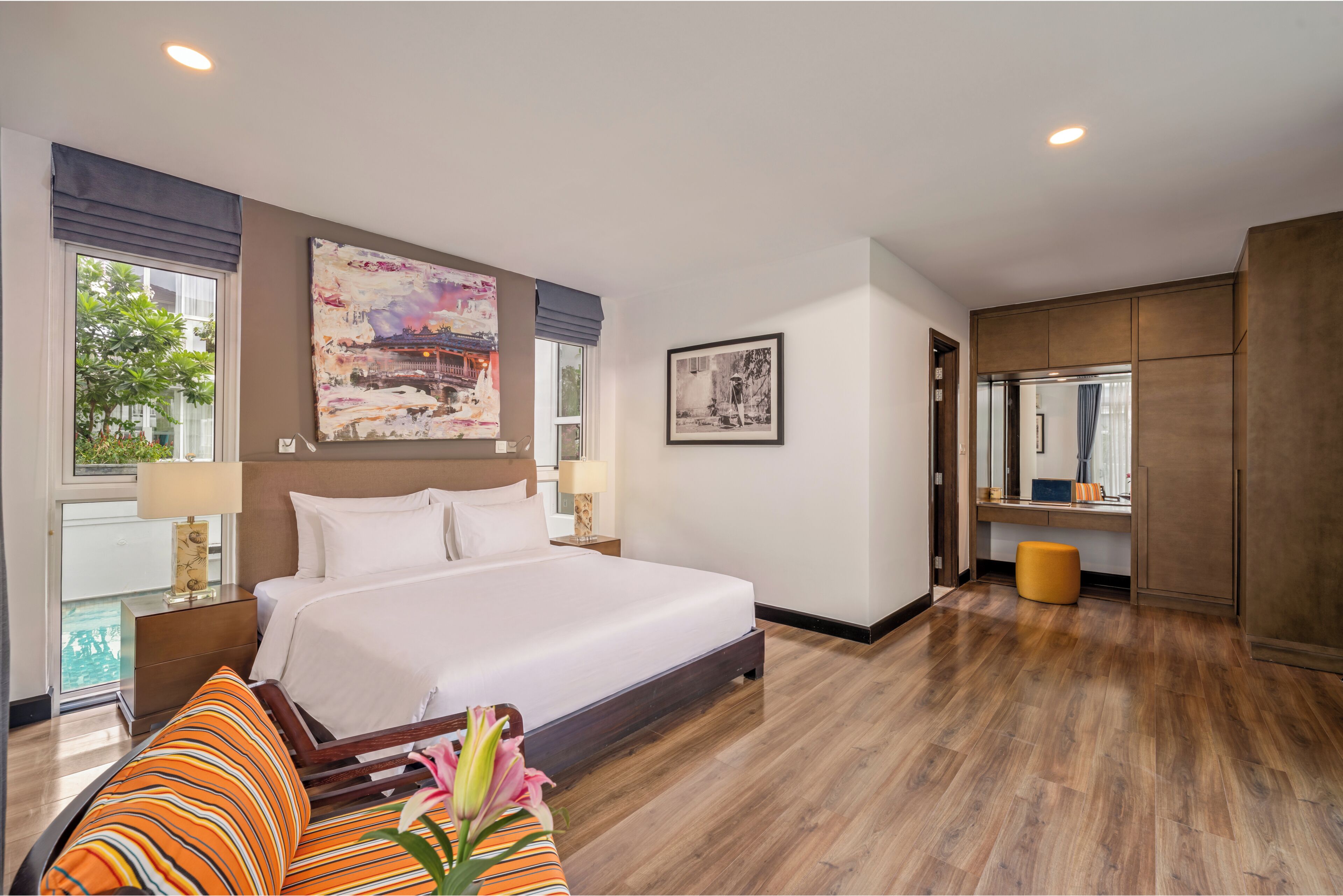 A hotel room with a large bed, a desk, a chair, and a window with a view of greenery.