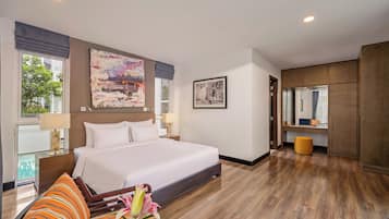 A hotel room with a large bed, a desk, a chair, and a window with a view of greenery.