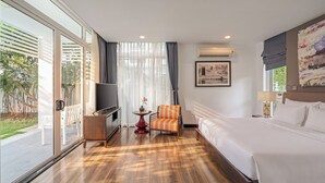 A hotel room with a bed, a TV, a chair, a small table with a vase, and a painting on the wall. - President Garden Ocean Villa  (Da Nang Municipality)