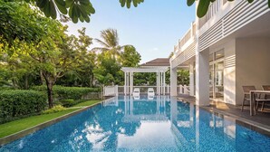 A swimming pool with a white pergola, surrounded by lush greenery and a modern building. - President Garden Ocean Villa  (Da Nang Municipality)