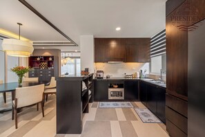 A modern kitchen with dark cabinetry, a central island, and a dining area with a table and chairs. - President Ocean Villa 840 sqm (Da Nang Municipality)