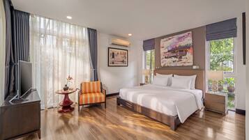 A hotel room with a large bed, a TV, a chair, and a window with a view.