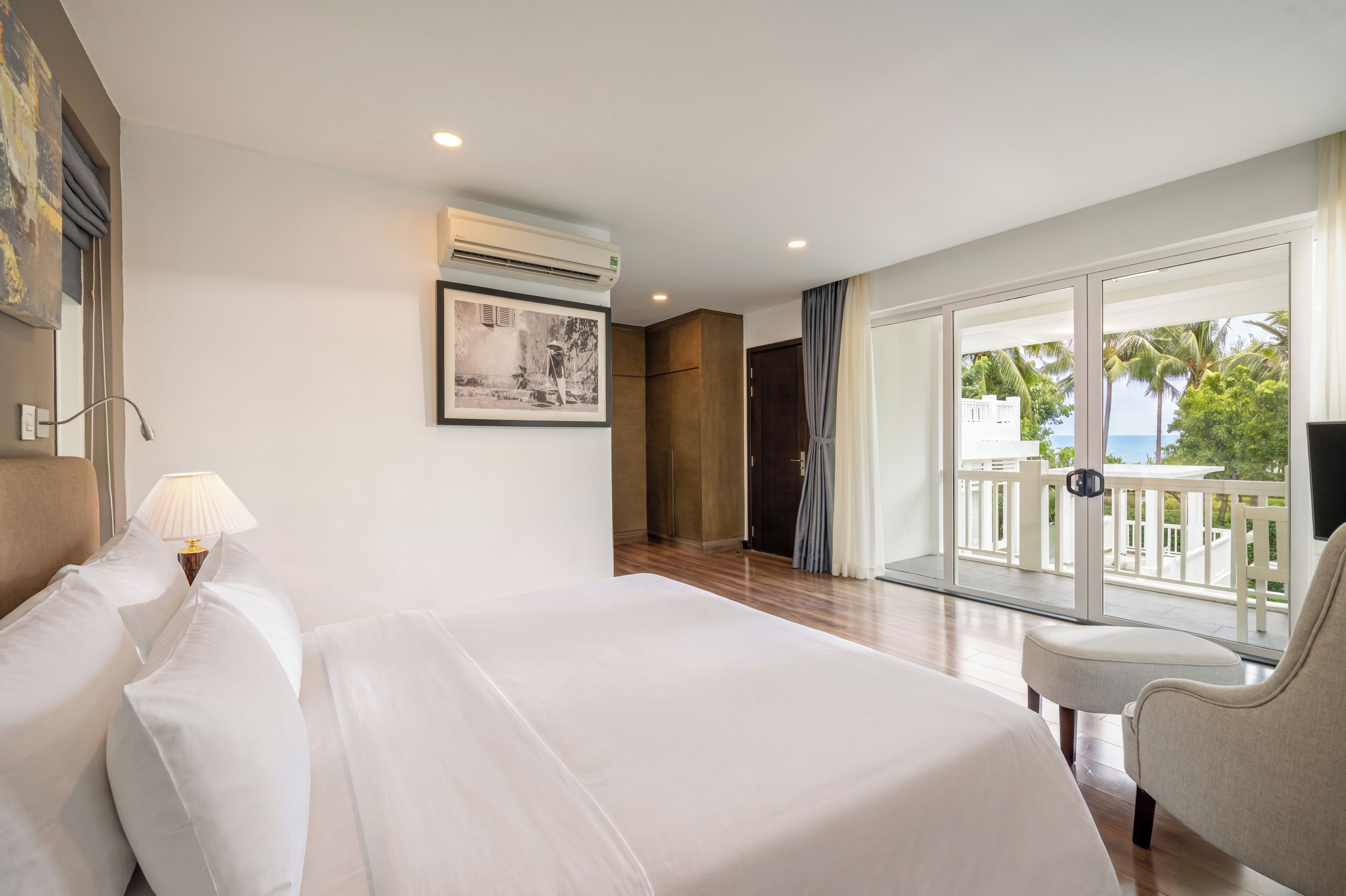Une chambre d’hôtel avec un lit, une chaise, un bureau, un appareil de climatisation, un tableau au mur et une vue sur l’extérieur.