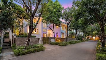 A modern two-story building with a paved driveway, surrounded by lush greenery and trees.