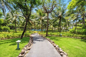 A pathway lined with palm trees and a well-maintained lawn, leading to a building with a white facade. - President Ocean Villa 840 sqm (Da Nang Municipality)