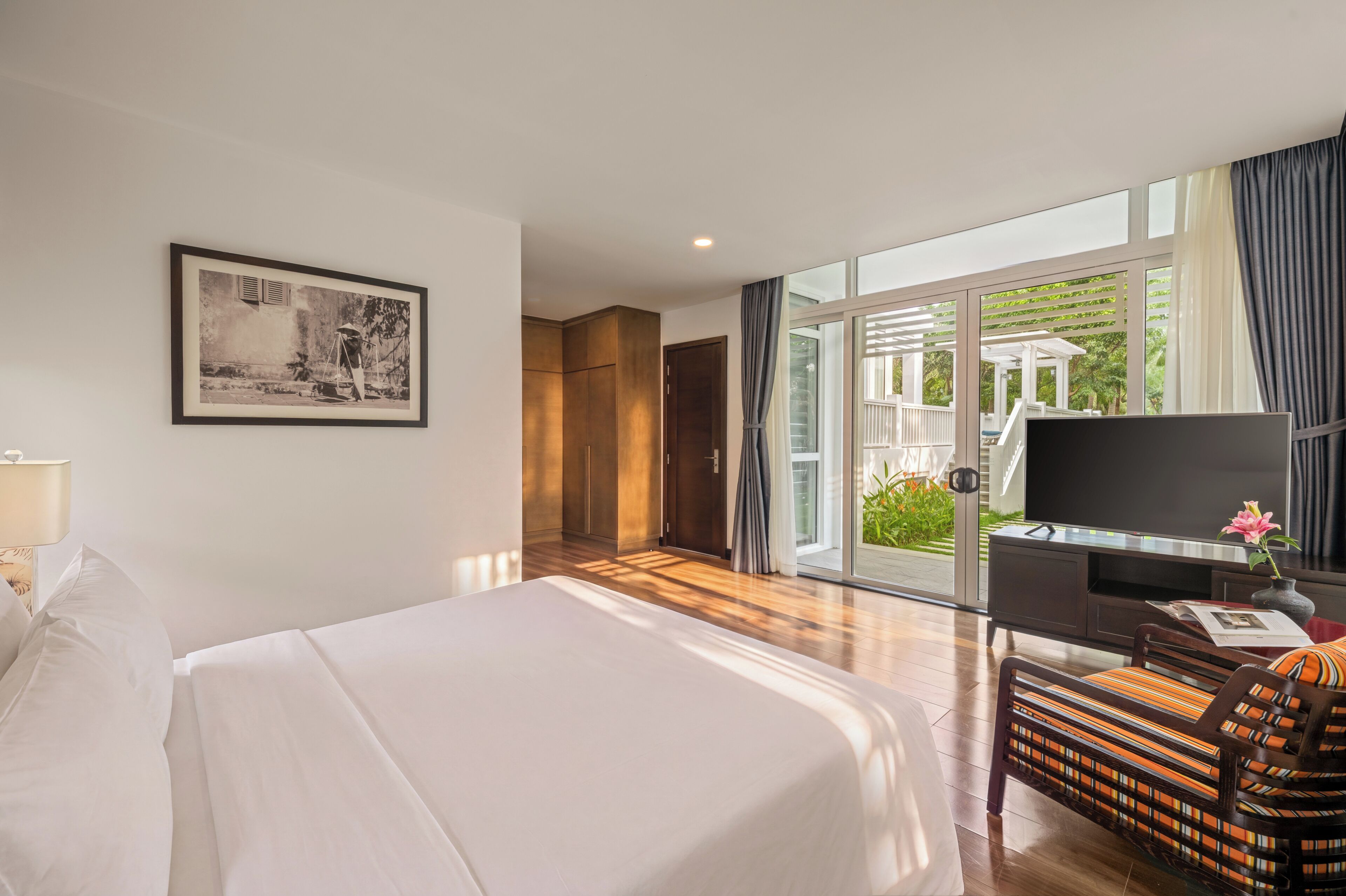 A hotel room with a bed, a desk with a TV, a chair, and a large window with curtains.