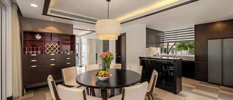 Un espace repas moderne avec une table ronde, des chaises, un lustre et une cuisine en arrière-plan.