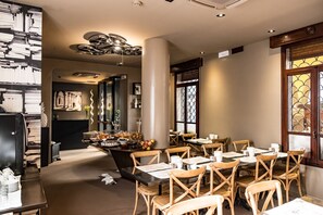 Een restaurantinterieur met houten stoelen, tafels en een decoratieve plafondlamp.