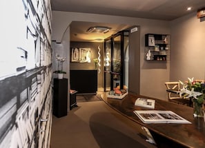 Een modern interieur met een lange houten tafel, een boekenkast en een decoratieve wand met een zigzaggend patroon.