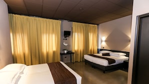 Une chambre d’hôtel avec deux lits, un bureau, une chaise, une télévision et des rideaux.