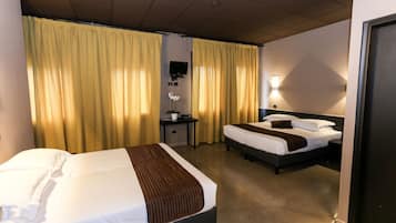 Quarto de hotel com duas camas, uma escrivaninha, uma cadeira, uma televisão e cortinas.