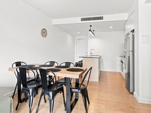 Une cuisine moderne avec un coin repas, comprenant une table en bois et des chaises noires, un îlot central intégré et des appareils électroménagers en acier inoxydable.
