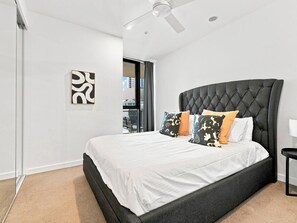 Ein modernes Schlafzimmer mit einem großen Bett, einem Deckenventilator und Blick ins Freie.